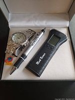 Photo of a silver-tone wristwatch with white dial, pen with flashlight, and black remote control device branded 'Mark Naimer' displayed on a light-colored surface inside a box.