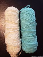 Two yarn bundles: one off-white and one light blue on a black surface.
