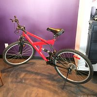 Full side view of red 21 speed mountain bike showing frame, saddles, tires, and crank area missing a pedal and crank.