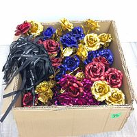 Box containing multiple 24K gold leaf roses in red, blue, gold, and pink colors with attached stems and black ribbons.