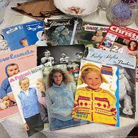 Photo showing assortment of vintage knitting books featuring baby and children's sweater patterns from brands like Patons and Monarch, lying on a table.