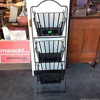 Full view of three black metal hanging baskets on vertical metal stand, showing their height and placement.