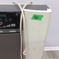 Side view showing the edge of the air purifier with power cord hanging and visible surface wear and discoloration.