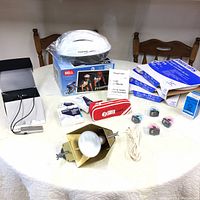 Overall view of all items on table: Bell white helmet, printer ink cartridges, Philips fluorescent light boxes, Swix ski wax pouch, hearing aid adapter, lamp fixture with bulb and cord.