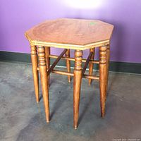 Front side view of a wooden vintage octagonal table with 8 legs, some spindle carvings on legs, showing wear on surface and edges