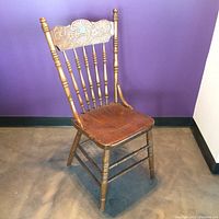 Full view of the vintage wooden chair highlighting carved backrest and turned spindle legs.