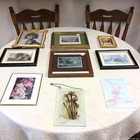 Collection of 10 framed and unframed art pieces on a table, showing vintage photos, botanical prints, and dried flower art.