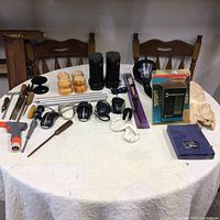 Overall view of all items on a white table including tower speakers, mice, tools, corded and cordless devices.