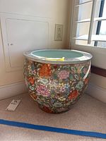 Photo showing full front view of the large ceramic planter with colorful hand-painted floral and bird designs placed near a wall outlet.