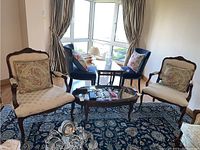 Two matching wooden armchairs with cream upholstery and floral cushions shown in living room setting with other furniture.