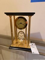 Front and side view of mantel clock showing brass columns, clock face with Roman numerals, and swiveling hourglass below.