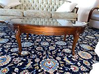 Front view of the wood coffee table showing the glass inset top and carved legs on a patterned rug.