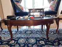 Side view of the wood and glass coffee table showing the carved legs and scalloped apron.