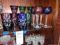 All colored stemware, clear cordials and footed bowl displayed on cabinet shelf