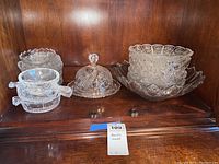 Crystal bowls and serving pieces displayed on wooden shelf including covered butter dish and large bowl
