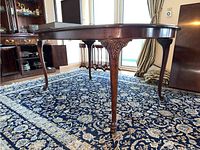 Side view of the oval dark wood Thomasville dining table with carved apron and legs on patterned rug