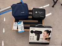 Lot displayed on black step board including blue Microlife blood pressure machine bag, black Lexus first aid kit pouch, Vivaspa percussion massager boxed, and universal walker glides.