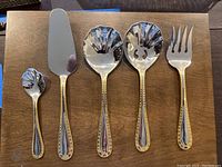 Full set of flatware utensils arranged side by side showing each piece clearly on wooden surface.