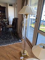 Full view of the floor lamp showing glass column, brass base and white shade in a room setting.