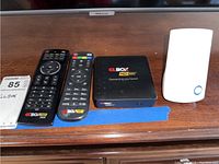 The GL Box HD 500 device seen with two remote controls and a TP-Link device on wooden surface.