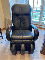 Front view of black leather massage chair showing seat, backrest, armrests, and foot/calf modules.