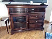 Front view of dark wood media console with glass inset door and three drawers beneath two open shelves.
