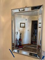 Photo showing full view of the rectangular beveled framed mirror hanging on the wall reflecting part of the room.