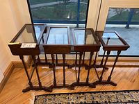 Set of four wooden nesting tables with glass tops placed side by side showing the overall size and design of the tables.