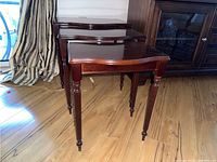 Three wooden nesting tables, dark polished finish, stacked one behind the other