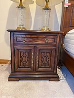 Front view of one wooden nightstand showing drawer and cabinet doors with brass handles.