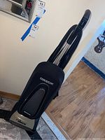 Full view of the upright vacuum cleaner showing black fabric bag and handle with control switch.