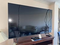 Front view of 65-inch Samsung TV on wooden console with cables draped over the screen.