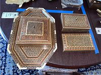 Three lidded boxes and octagonal tray with intricate geometric and floral inlay patterns on table.