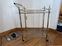 Full view of bar cart showing metal frame and bottom glass shelf on caster wheels.