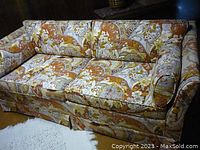 Front-facing photo of the sofa bed showing full sofa with colorful floral and paisley upholstery in warm tones indoors on a light rug.