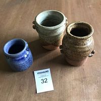 Three Bodil Pearson studio pottery pieces in varying glazes and shapes on a wooden surface