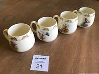 Four Royal Doulton Bunnykins bone china mugs displayed in a row on wooden surface, showcasing the different Bunnykins patterns around the mug body and rim.