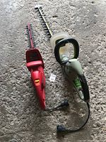 Photo of two electric hedge trimmers side by side on ground showing overall design and electric cords.