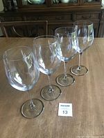 Four clear Luigi Bormioli Rocco wine glasses standing in a row on a wooden table.