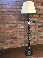 Full view of the floor lamp showing height, base, and shade against a brick wall.