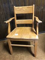 Front view of a solid oak armchair showing wood grain, wide armrests, and backrest slats.