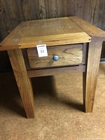 Close-up photo showing one solid oak end table with a drawer, metal knob, and visible wood grain, showing overall construction and condition.