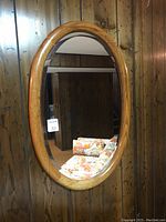 Full view of the solid oak oval framed mirror hung on a wood-paneled wall showing its size and shape.