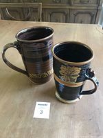 Two ceramic pottery jugs side by side on wooden table showing height, shape, and color patterns of the jugs.