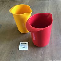 Two brightly coloured melamine pitchers, one red and one yellow, shown side by side on wood surface with MaxSold tag