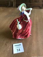 Full view of the Royal Doulton figurine showing the lady in a red flowing dress and white bonnet with a handbag.