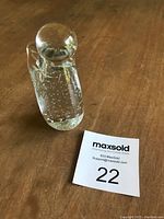 Clear glass angel figurine on wooden surface with MaxSold lot number card