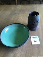 Photo of the green glazed pottery bowl and black carved candle holder displayed on a wooden table with lot number card.