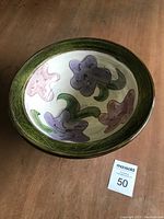 Top view of a round ceramic bowl with purple and pink flower leaf pattern inside and green rim with carved details.