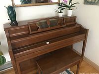Front view of vintage upright mahogany piano with matching bench under it. Polished finish and straight legs.